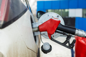 Red fuel nozzle inserted into dirty white car tank at gas station in winter, close-up view highlighting refueling process and everyday vehicle use.