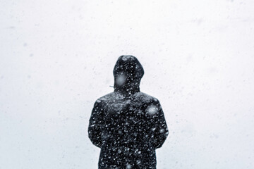 Solitary person in hooded coat faces heavy snowfall on pale background, bleak winter mood with copy space for weather safety message.