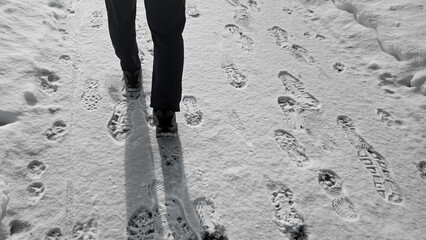 Winter walk. A person's boots leaving fresh footprints in on a snow trail, a sunny day scene. Fitness or journey abstract concept background.