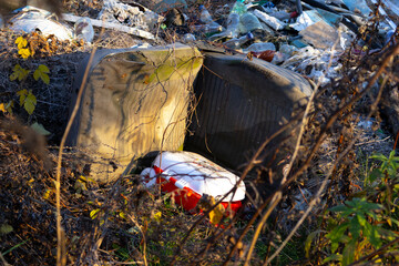 Trash scattered in a neglected area with an old couch and a red item visible among the debris during daylight hours
