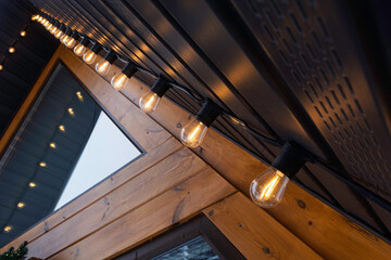 Warm string lights on A-frame house facade emphasize triangular roof lines and wooden texture, creating cozy evening mood for cabin living