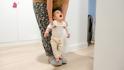 Baby standing with mother support in cozy home setting