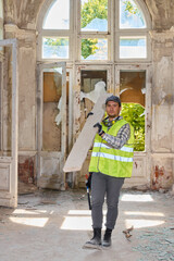 Man with reflective gear carrying timber across dilapidated hall