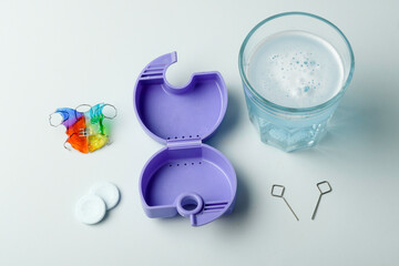 Dental expander retainer kit with open purple case, two expansion keys, effervescent tablets, water glass on light blue background.