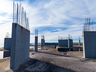 Construction site shows pillars and foundations under a blue sky near a water body in a developing area during an overcast day