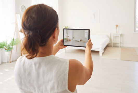 Back view of rental agent or female realtor taking photo on tablet of stylish home bedroom interior planning to sell apartment. Woman house seller making video call to client showing room