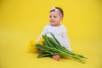 little girl in white dress on yellow background. Cheerful happy child with tulips flower bouquet
