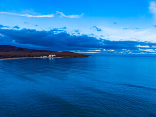 View of calm water and distant land under cloudy sky near coastline at sunset with light reflecting on surface