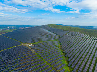 Solar panels cover a hillside in a renewable energy project under a blue sky with scattered clouds in a rural area
