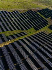 Solar panels are arranged in rows on farmland in a hilly area during daylight hours for renewable energy production