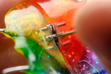 Close hand tightens metal screw of glitter rainbow palatal expander retainer, macro detail with soft blur clinical background.