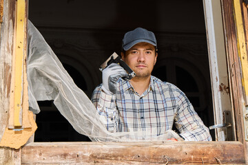 Man in work clothes checks old window frame during renovation
