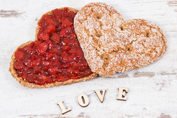 Fresh baked bread in shape of heart with strawberry jam and inscription love. Rustic background