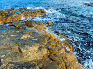 Waves crash against rocky shoreline at the ocean during daylight hours near the coast