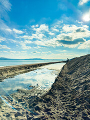 Clouds float above a wide beach with calm water in the distance and a small group of people near the pier during the late afternoon