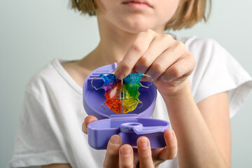 Child carefully stores colorful orthodontic retainer in purple case for daily hygiene to keep dental appliance clean and safe at home.