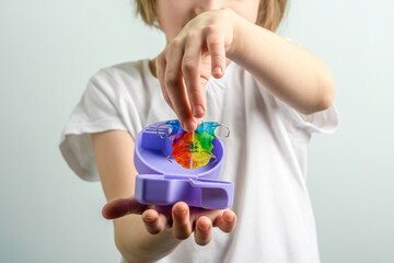 Young child places colorful orthodontic retainer into open purple travel case to protect removable dental appliance between uses.