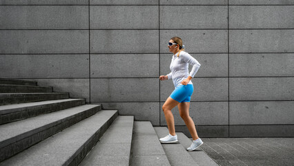 Beautiful middle-aged woman running up concrete stairs against background of concrete wall in city on summer day. Side view	