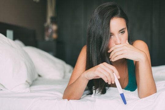 Woman reflecting on pregnancy results in bedroom