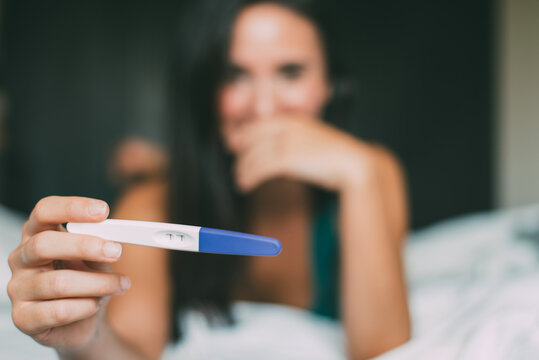 Woman holding pregnancy test while lying in bed