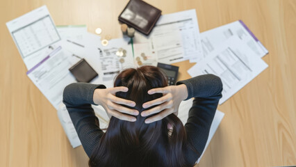A woman overwhelmed by paperwork on a wooden desk viewed from above