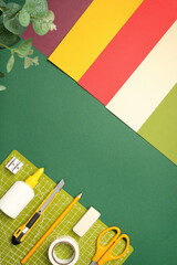 Flat lay of craft supplies. Colored paper, cutting mat, scissors, pencil, tape, craft knife on green background. Copyspace