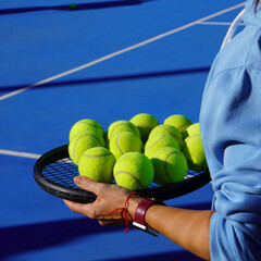 Tennis lessons concept. Person in sportswear and smartwatch collecting tennis balls during their lessons on a sunny day