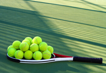 Tennis concept. A racket resting on a green court with a pile of tennis balls on it.