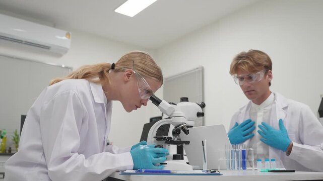 Research team examines samples under microscope in laboratory setting with clear focus on analysis