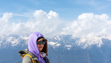 Woman hiker with backpack and sunglasses standing on snowy mountain viewpoint enjoying panoramic landscape against blue sky and snow-covered peaks Travel, hiking, active lifestyle concept copy space