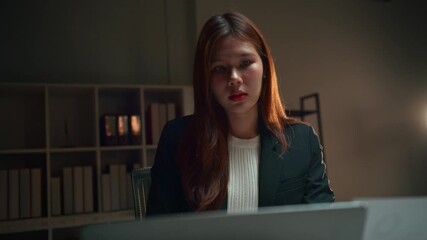 Determined asian businesswoman focusing on her laptop screen. Hardworking professional female staying late in a modern office at night