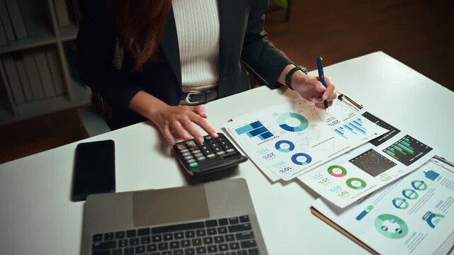 Professional businesswoman analyzing financial charts and graphs. Accountant using a calculator to check company budget and investment data