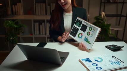 Young Asian professional woman working late at night, presenting financial data and charts to colleagues during a virtual online meeting - Powered by Adobe