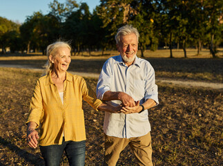 Happy active senior couple having fun talking holding hands and bonding in park outdoors