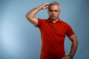Mature handsome man wearing casual t-shirt over blue background confuse and wondering about question. Uncertain with doubt, thinking with hand on head. Pensive concept.