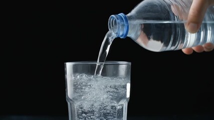 Clear water being poured from a plastic bottle into a transparent glass, with bubbles forming in the glass against a dark background - Powered by Adobe