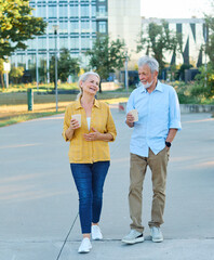 Happy active senior couple having fun talking drinking coffee and bonding in park outdoors