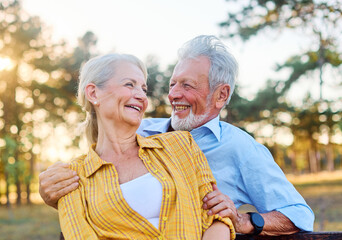 Happy active senior couple having fun talking and hugging sitting on a bench in park outdoors