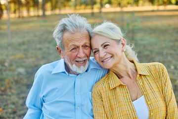 Happy active senior couple having fun talking and hugging sitting on a bench in park outdoors