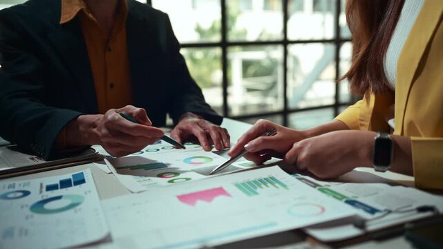 Two business professionals analyzing documents with charts and graphs. Colleagues pointing at data sheets discussing corporate strategy
