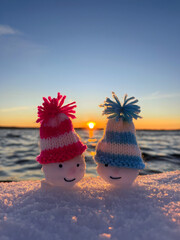 cute snowman with knitted hats on the winter beach in sunset