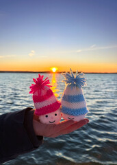 hand holding cute snowman with knitted hats on the winter beach in sunset