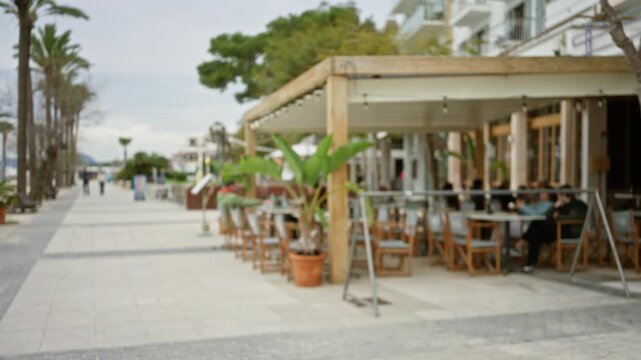Blurred view of people walking along a mediterranean promenade in mallorca with a defocused outdoor cafe and bokeh effect enhancing a relaxing atmosphere.