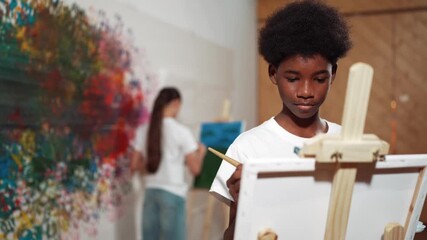 African boy painting canvas with watercolor while happy caucasian girl draw cool tone picture at colorful stained wall. Multicultural high school student attend creative activity together. Edification