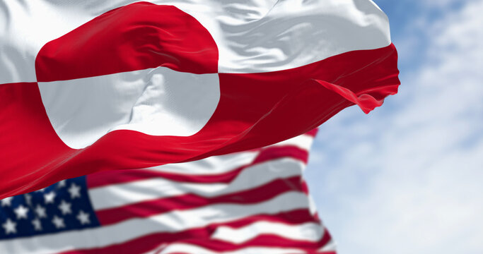 Flags of Greenland and the US waving in the wind on a clear day