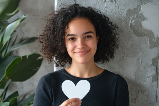Cheerful girl holding a heart cutout indoors with greenery in the background