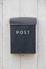 a black, old, scratched mailbox on a wooden fence
