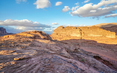 Afternoon sun shines on rocky formations in Wadi Rum desert, blue sky with few clouds