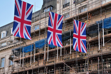 British Union Jack flags hanging above main street in London after king coronation, scaffolding on a building at background
