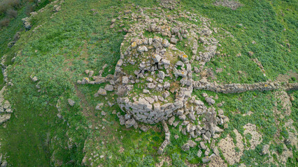 Prehistoric nuraghe stone structure rising from green landscape under dramatic sky in Sardinia